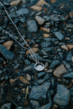 Load image into Gallery viewer, Silver Mount Crested Butte necklace with a pendant on pebbles
